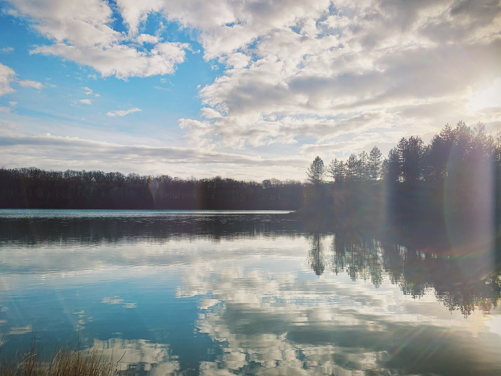 Calm lake reflecting clouds and trees in the Gers countryside